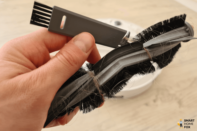 Haare werden aus der Hauptbürste des ECOVACS DEEBOT T10 mit Hilfe des beigefügten Reinigungswerkzeugs entfernt.